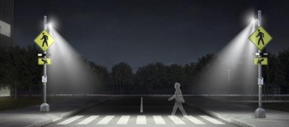 SafeWalk crosswalk illuminators mounted on two poles lighting a pedestrian at a midblock crosswalk at night